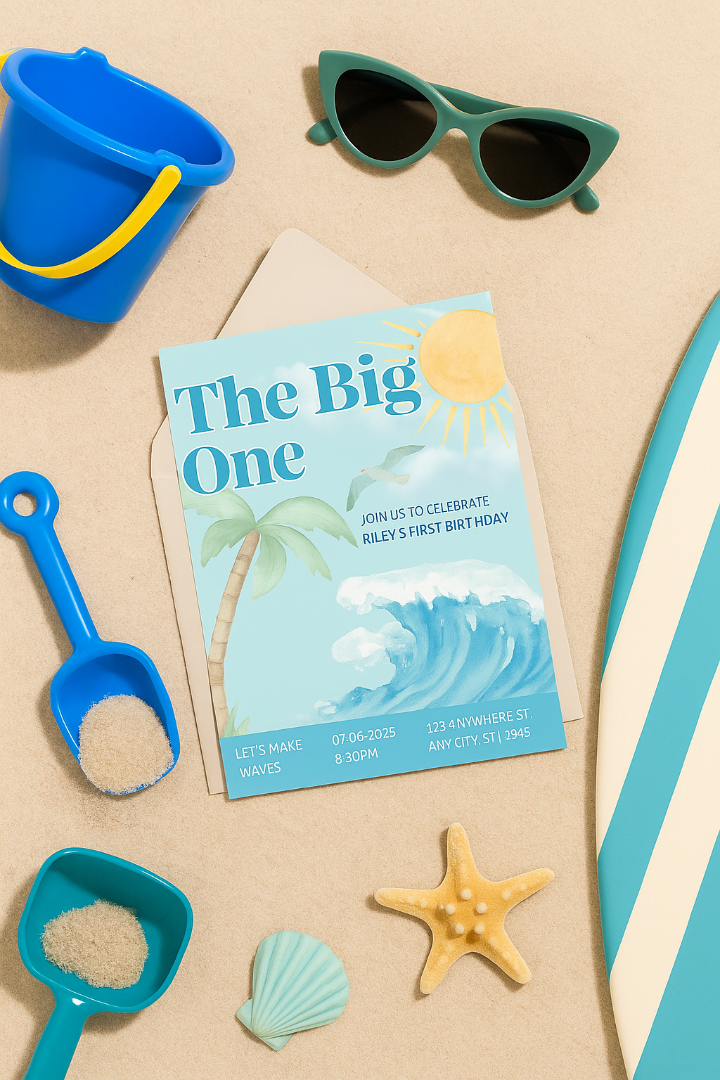 Beach-themed flat lay for a first birthday party. Features a party invitation reading “The Big One,” styled with sand, a palm leaf, seashells, a starfish, sunglasses, and a corner of a surfboard. A fun and summery surfer vibe.