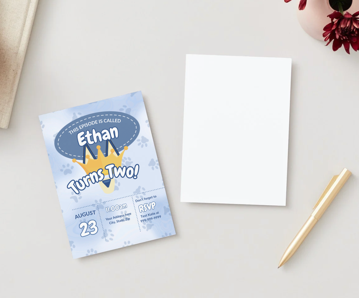 Flat lay of a Bluey-inspired birthday invitation for “Ethan Turns Two!” placed on a neutral surface with a blank white card, gold pen, and flower vase. The invite features a crown, paw prints, and event details for August 23 at 11:00 AM with RSVP info.