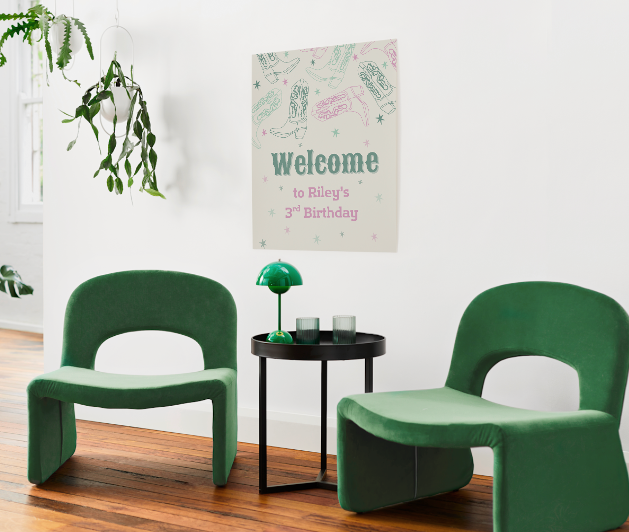 Western cowgirl-themed birthday welcome sign on a white wall above green velvet chairs and black table. Sign features pastel cowboy boots and stars with text “Welcome to Riley’s 3rd Birthday.” Perfect party signage mockup in modern interior setting.